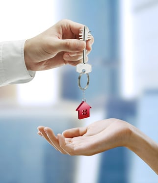 Real estate agent handing over house keys with red house keychain to new tenant or buyer
