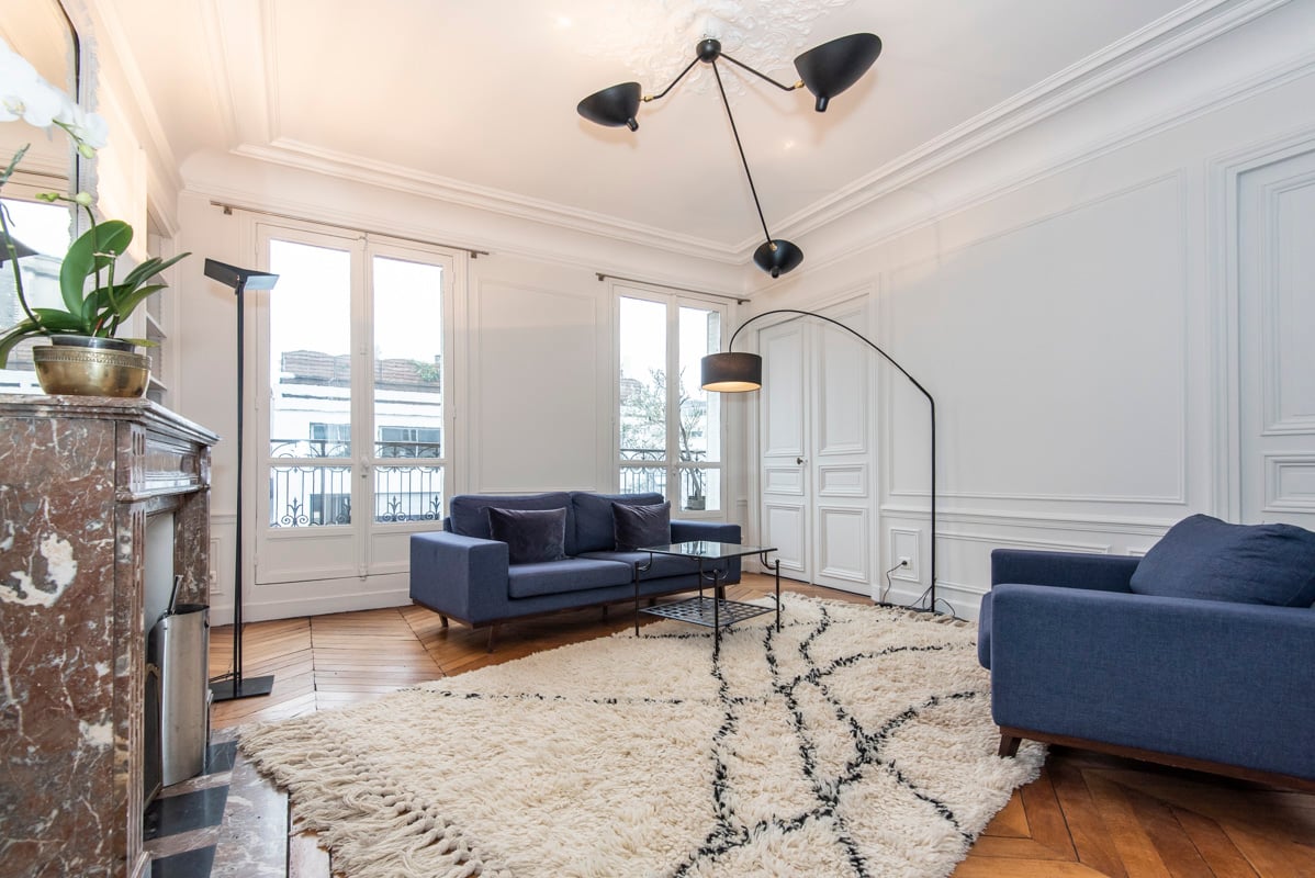 Salon Haussmannien élégant aux plafonds hauts, portes-fenêtres, luminosité généreuse, mobilier design et vue panoramique sur la ville depuis balcon privé.