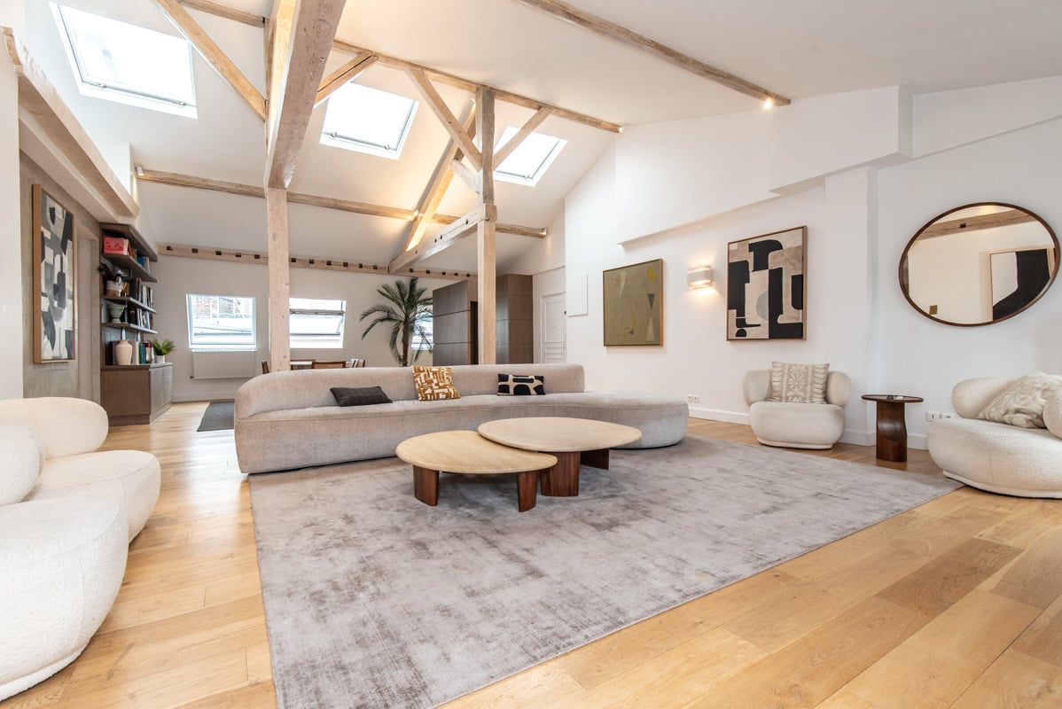 Luxury loft with exposed wooden beams, skylights flooding natural light, designer furniture, and open-plan living space. Premium architectural finishes.