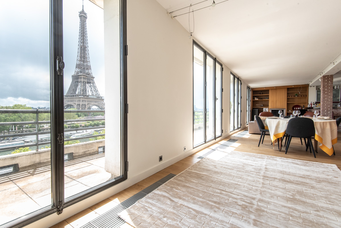 Luxury Parisian apartment with panoramic Eiffel Tower views, floor-to-ceiling windows, soaring ceilings, and sophisticated dining space flooded with natural light.
